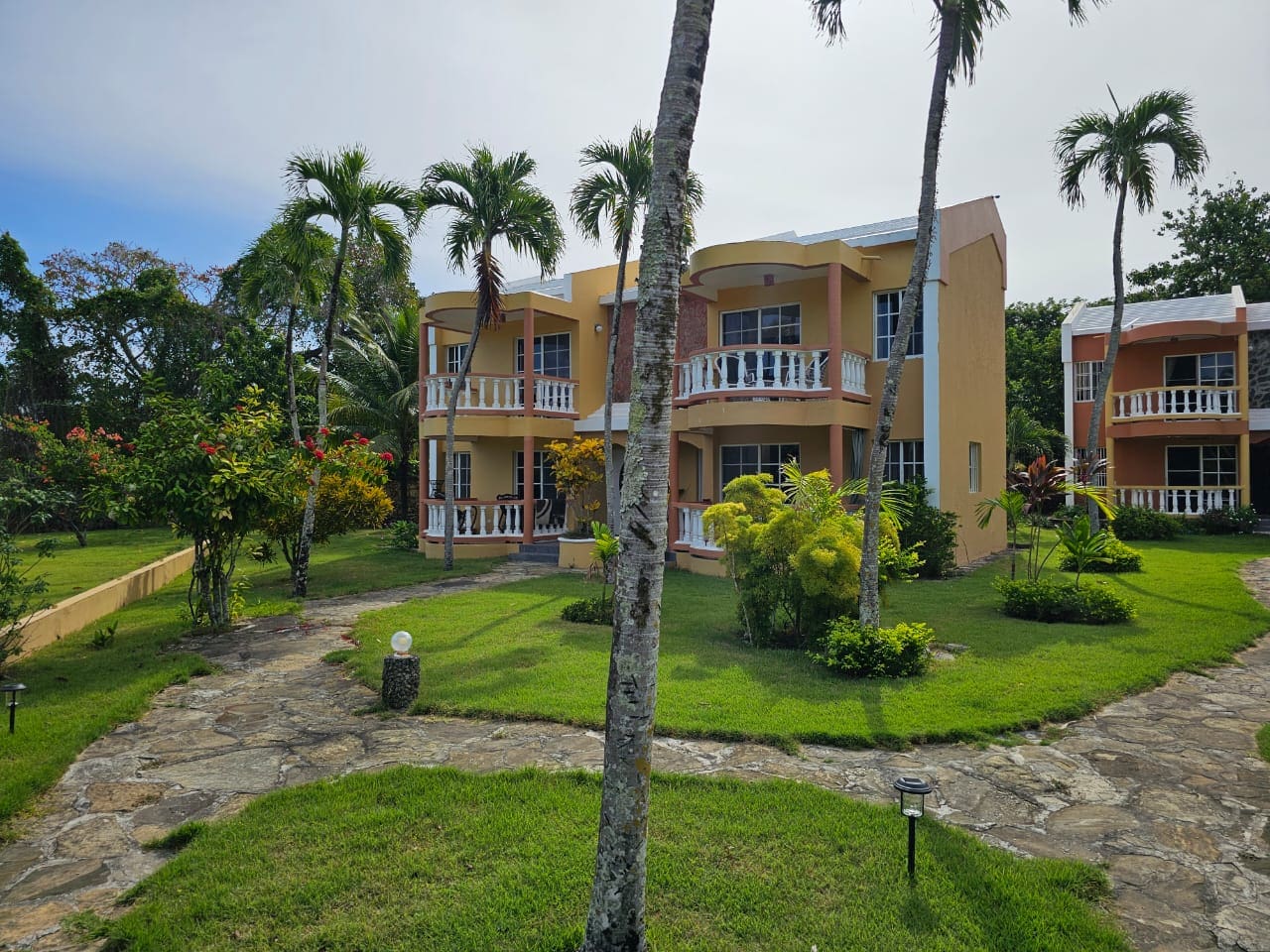 buyDRproperty Exterior view of a Great Condo for Sale near SOSUA Center, with palm trees and stone pathway. Sosua Real Estate