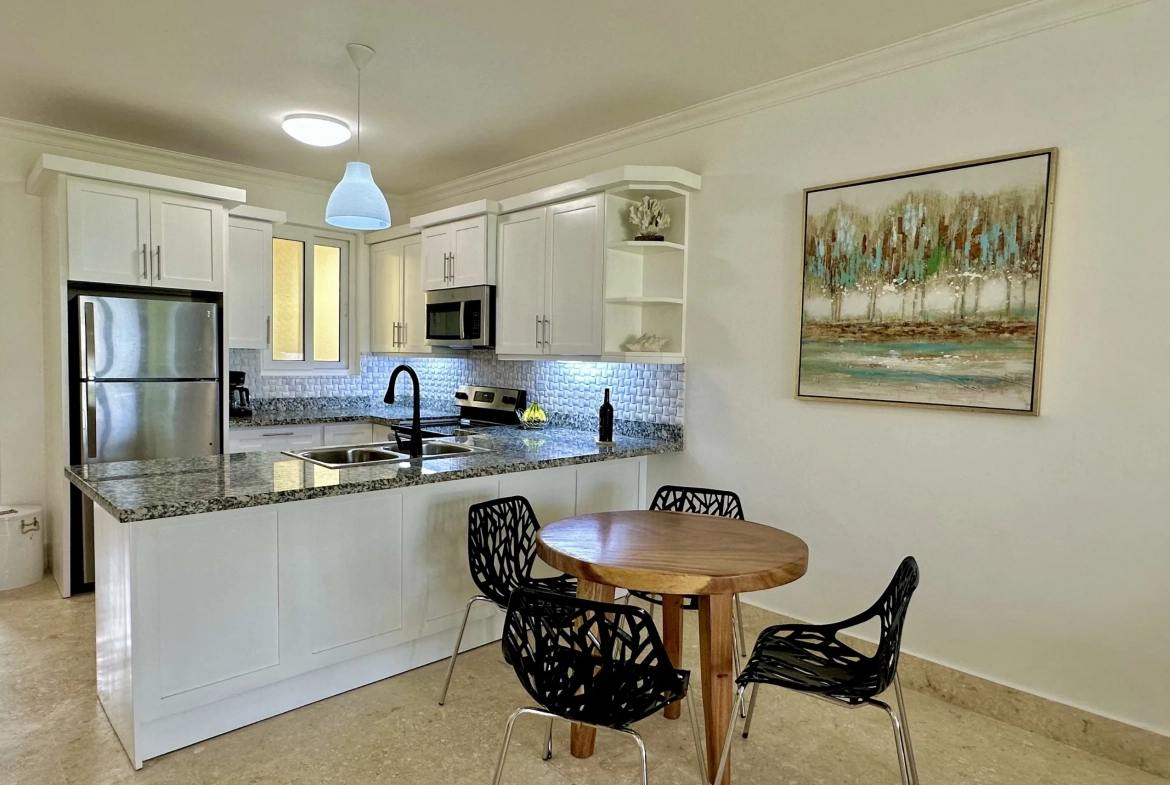 buyDRproperty Modern kitchen and dining area in a 2-Bedroom Condo with granite countertops and black chairs. Sosua Real Estate
