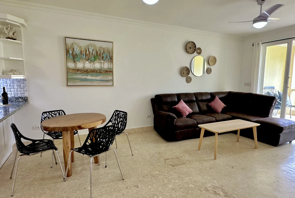 buyDRproperty Living room of a 2-bedroom condo with brown leather sectional and modern dining table. Sosua Real Estate