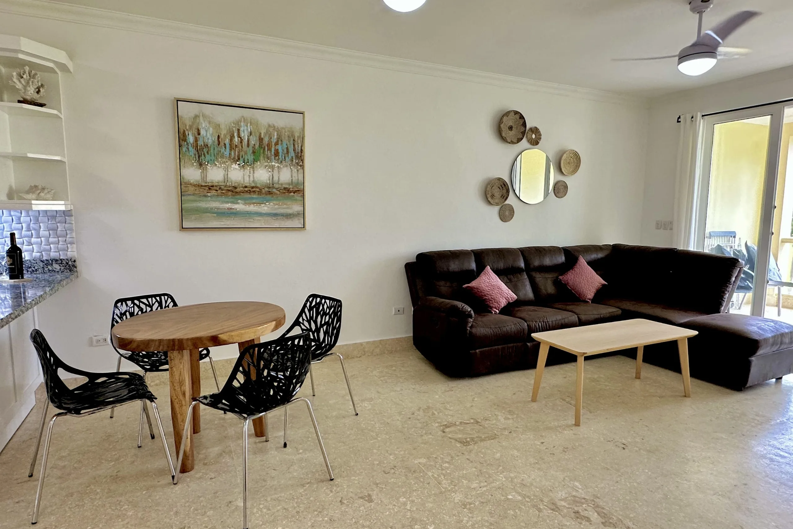 buyDRproperty Living room of a 2-bedroom condo with brown leather sectional and modern dining table. Sosua Real Estate