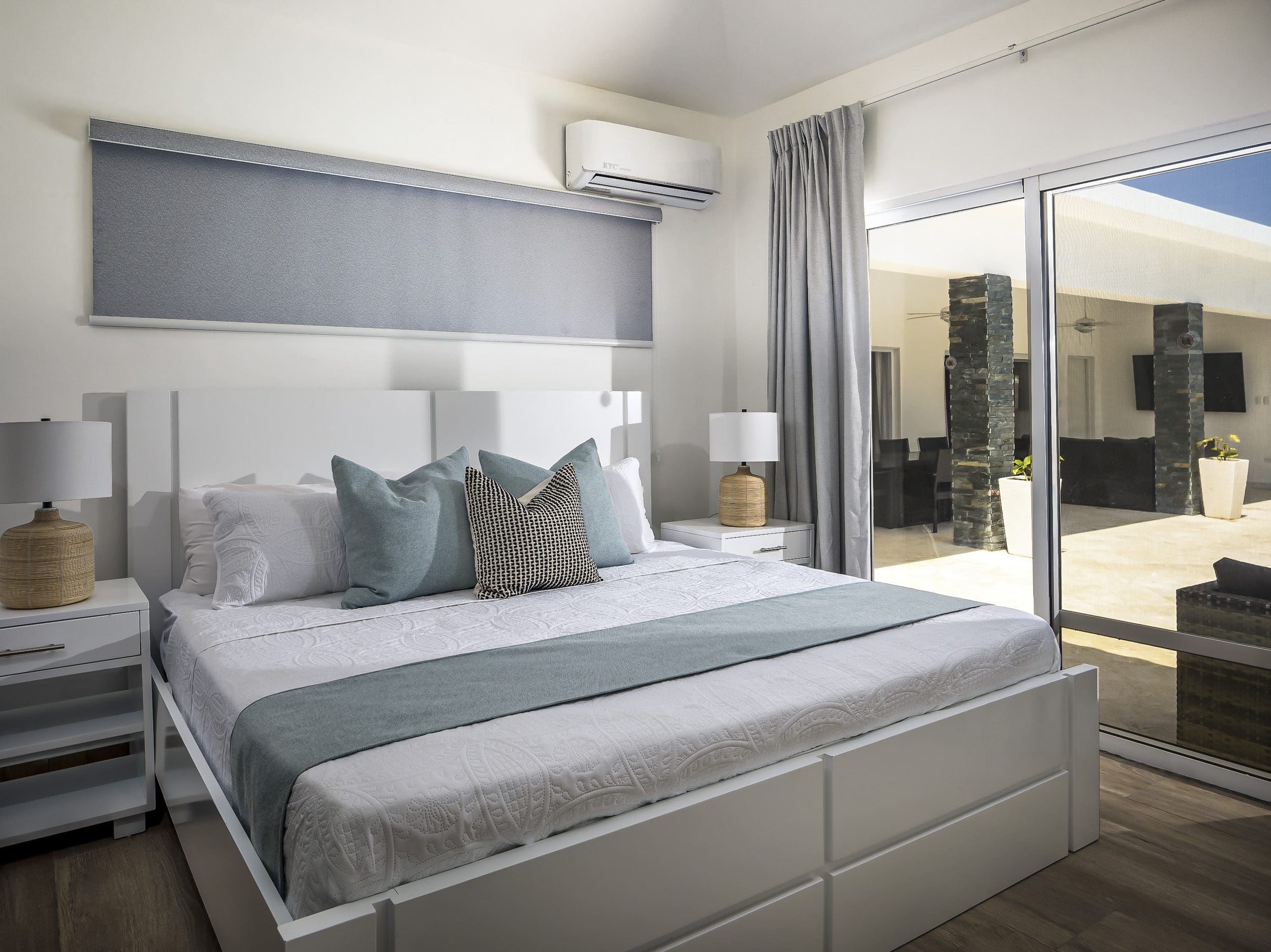 buyDRproperty Modern bedroom in a Villa For Sale in Casa Linda. White bed with teal accents and sliding glass doors. Sosua Real Estate