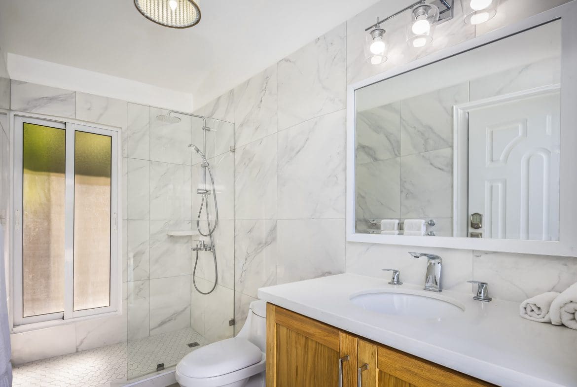 buyDRproperty Modern bathroom with marble tile, glass shower, and wooden vanity. Villa For Sale in Casa Linda. Sosua Real Estate
