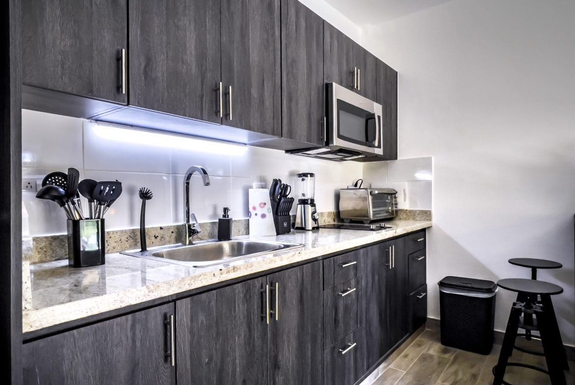 buyDRproperty Modern kitchen in a one-bedroom condo for sale in Sosua, featuring dark wood cabinets and stainless steel appliances. Sosua Real Estate