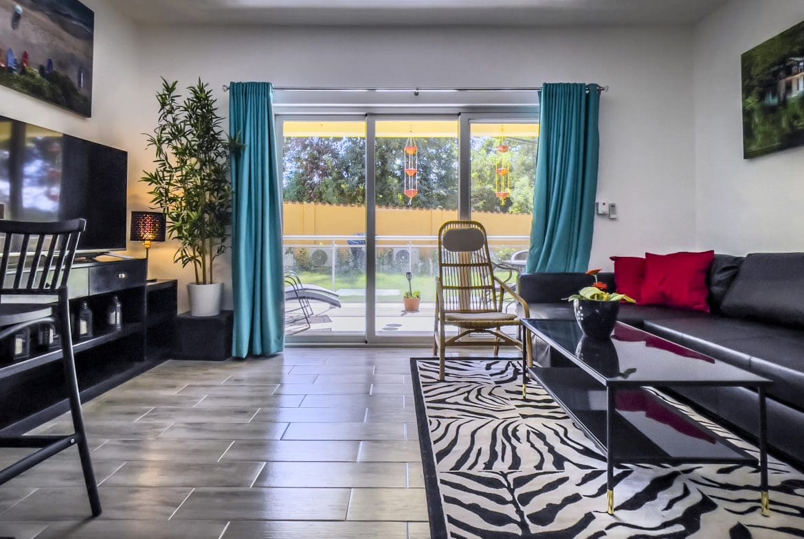 buyDRproperty Living room of a one-bedroom condo with black sofa, zebra rug, and teal curtains. Sosua Real Estate