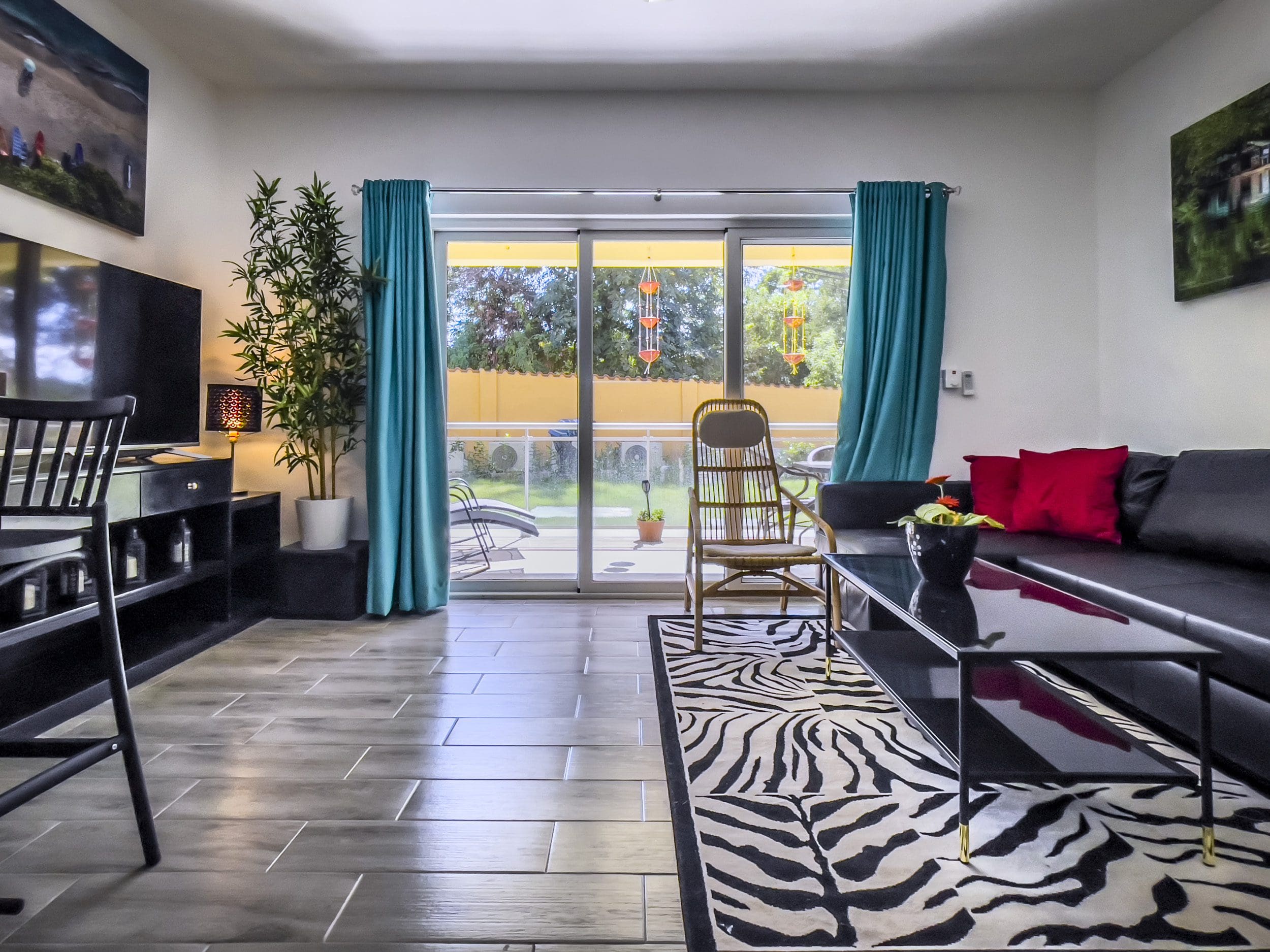 buyDRproperty Living room of a one-bedroom condo with black sofa, zebra rug, and teal curtains. Sosua Real Estate