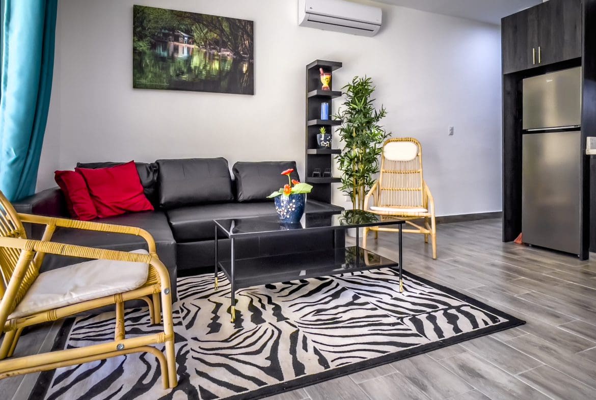 buyDRproperty Living room in a one-bedroom condo featuring a black sofa, bamboo chairs, and zebra rug. Sosua Real Estate