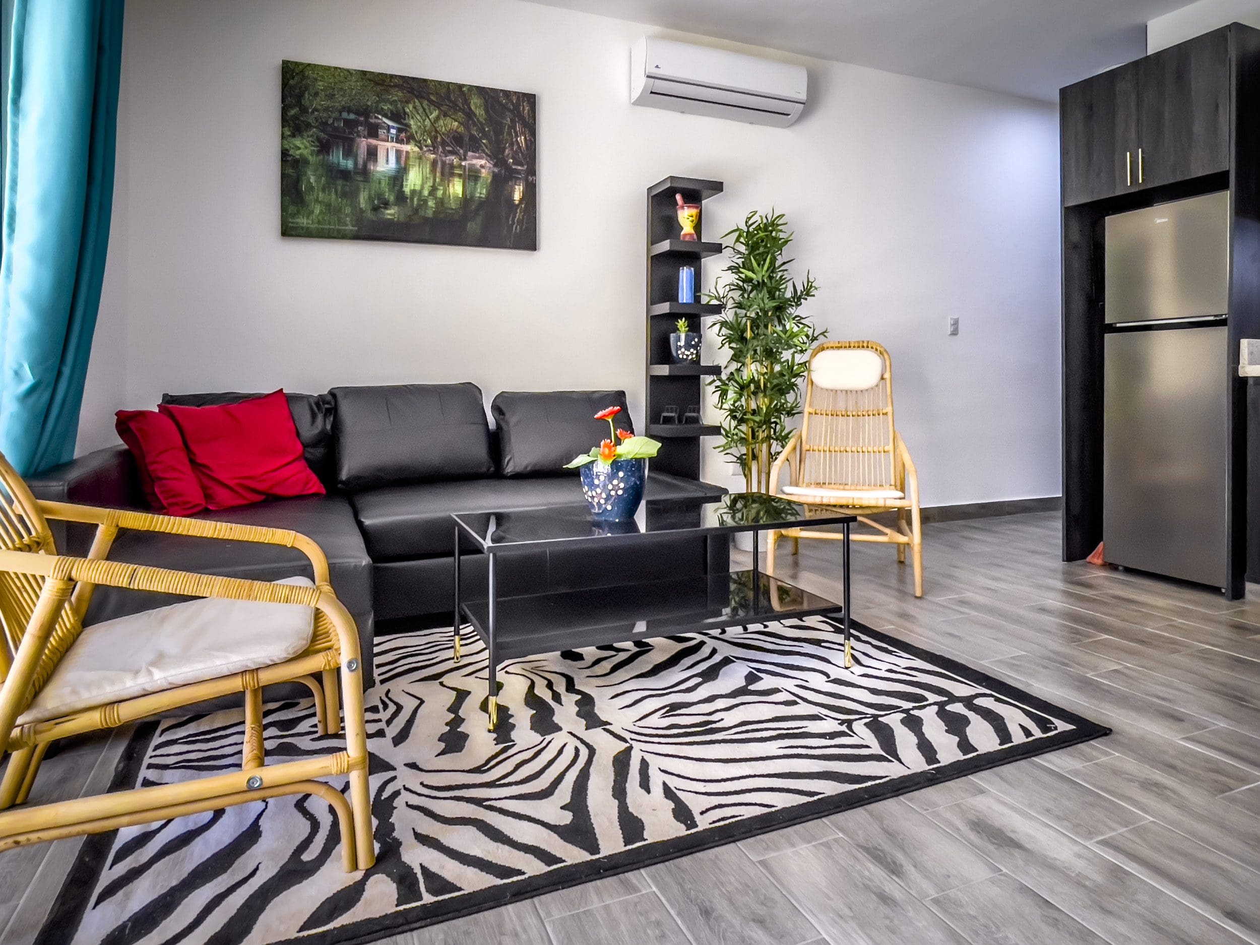 buyDRproperty Living room in a one-bedroom condo featuring a black sofa, bamboo chairs, and zebra rug. Sosua Real Estate