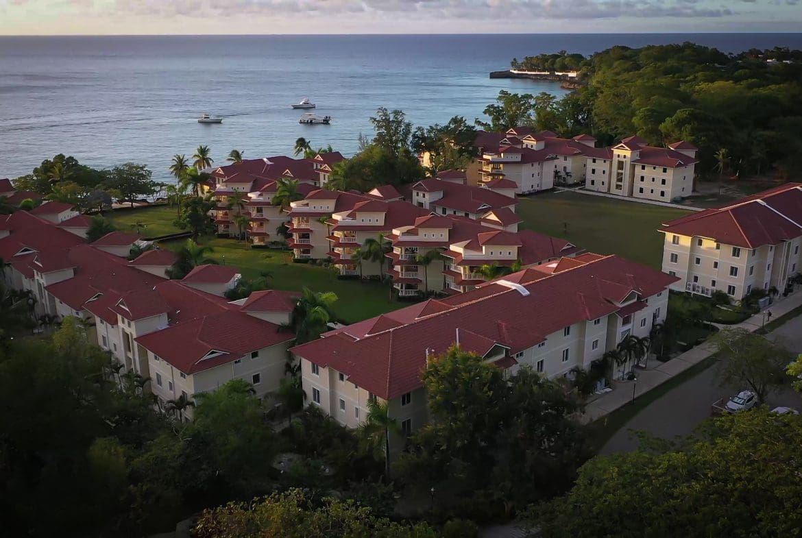 buyDRproperty Aerial view of a 2-Bedroom Condo complex near the ocean with red roofs. Sosua Real Estate