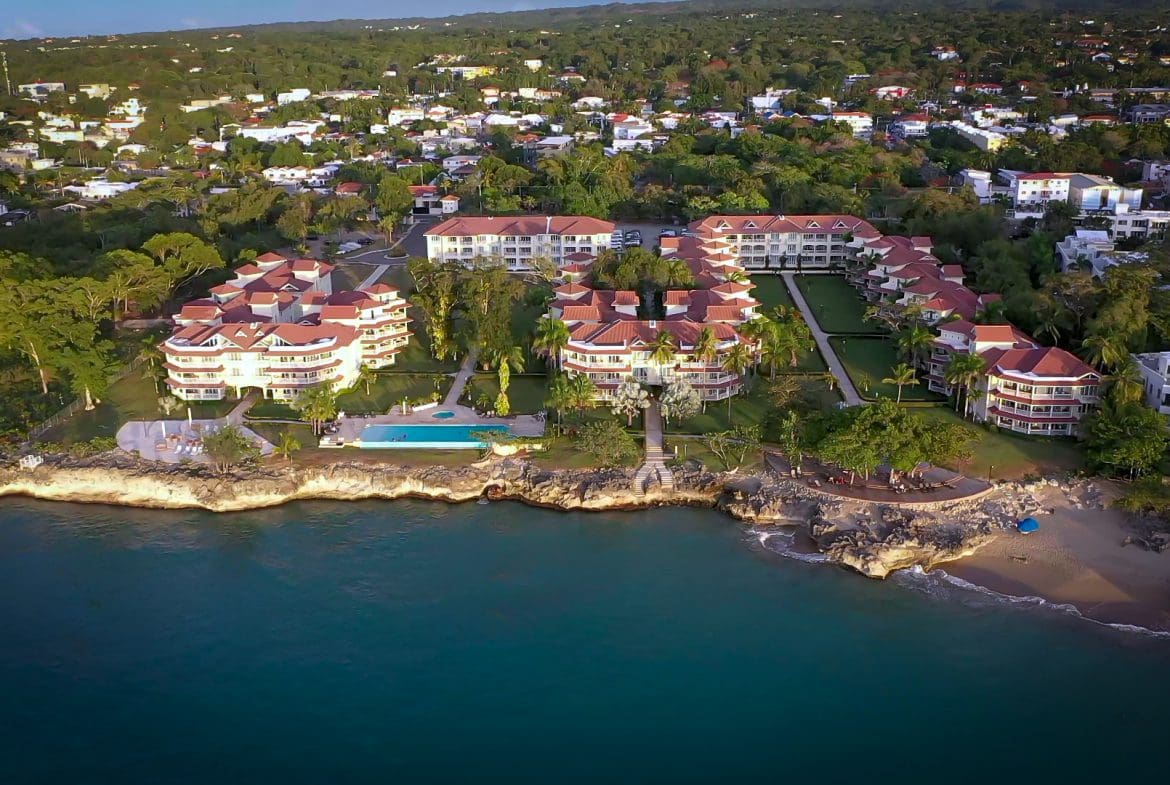 buyDRproperty Aerial view of a 2-bedroom condo in Hispaniola Beach, showcasing resort buildings, pool, and beach. Sosua Real Estate