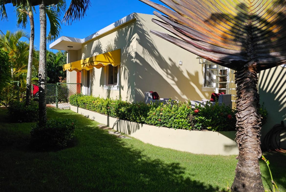 buyDRproperty Casa Linda Villa with yellow awning, surrounded by lush greenery Sosua Real Estate