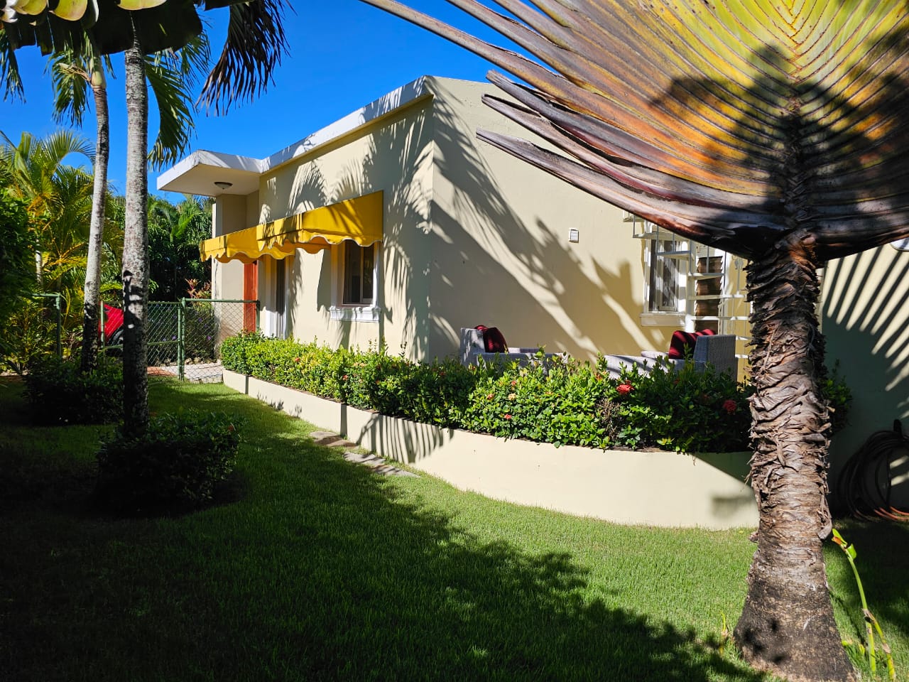 buyDRproperty Casa Linda Villa with yellow awning, surrounded by lush greenery Sosua Real Estate