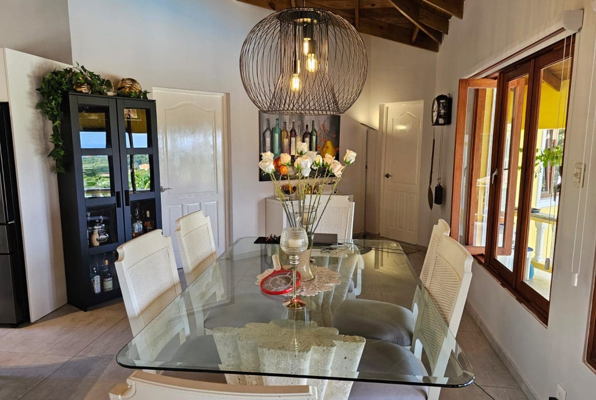 buyDRproperty Dining area in luxury villa with ocean views, featuring glass table, white chairs, and modern lighting. Sosua Real Estate