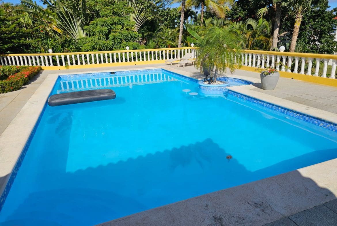 buyDRproperty Swimming pool at a luxury villa with ocean views, surrounded by lush tropical plants. Sosua Real Estate