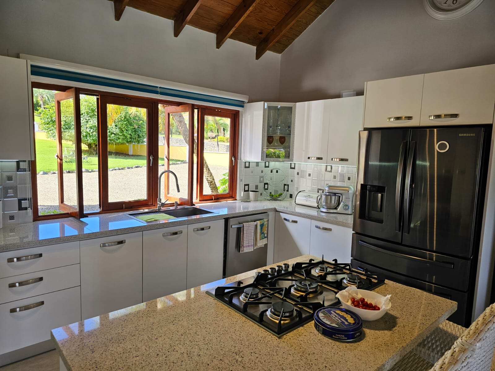 buyDRproperty Modern kitchen with island gas cooktop and window showing lush outdoor view of a luxury villa. Sosua Real Estate