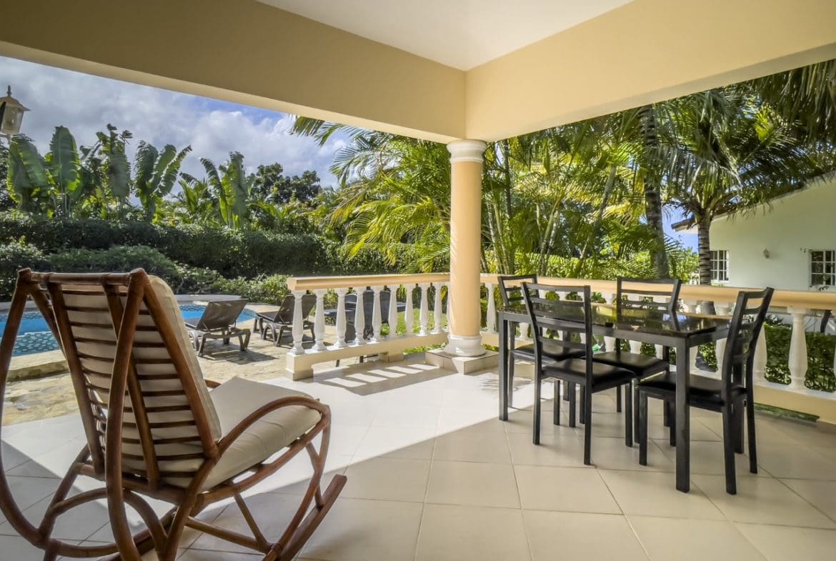buyDRproperty Covered patio with dining table and rocking chair overlooking pool and tropical foliage. 3BR Ocean View Home Sosua Real Estate