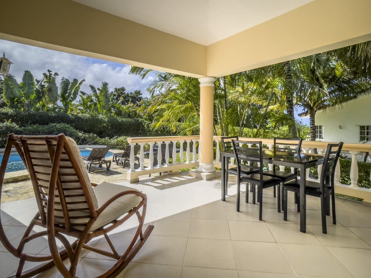 buyDRproperty Covered patio with dining table and rocking chair overlooking pool and tropical foliage. 3BR Ocean View Home Sosua Real Estate