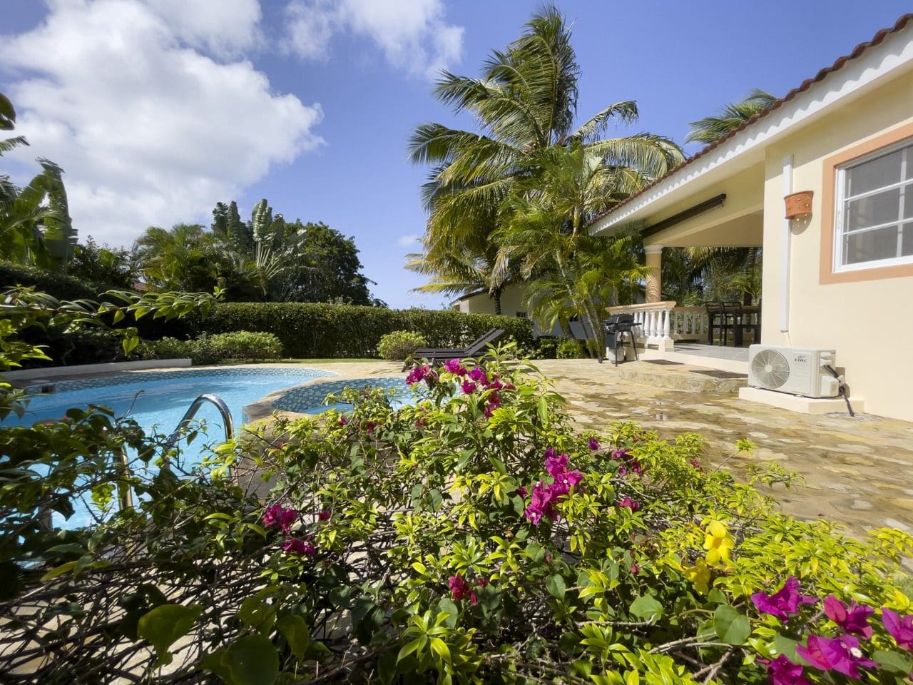 buyDRproperty Poolside view of a 3BR Ocean View Home in Hispaniola, lush tropical garden, and blue sky. Sosua Real Estate
