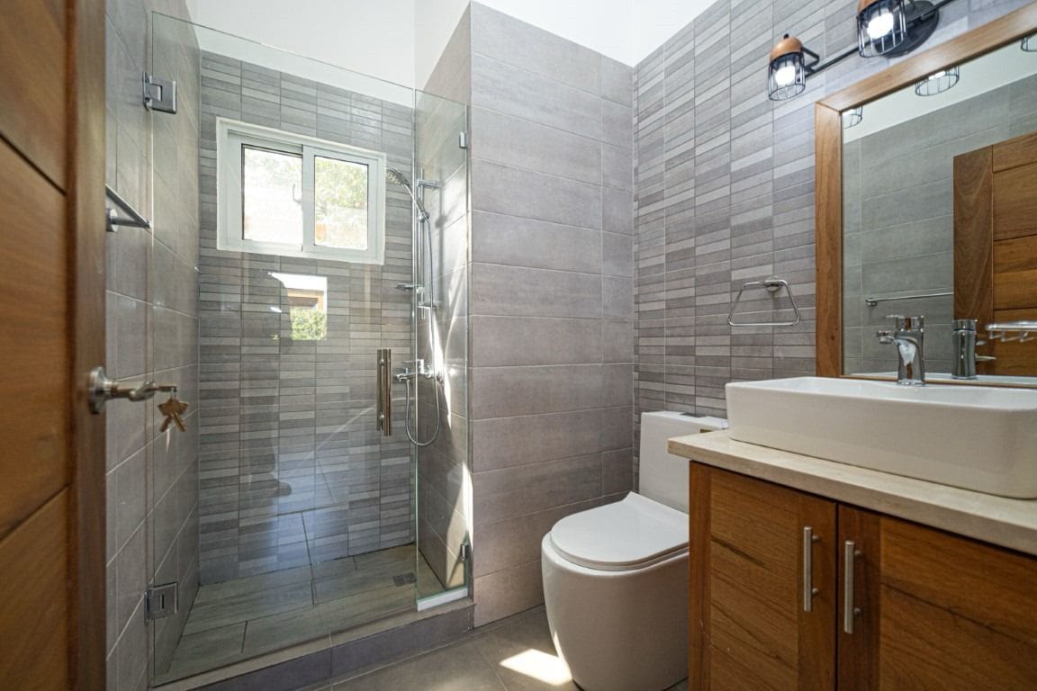 buyDRproperty Modern bathroom with gray tile, glass shower, and wooden vanity. Home for Sale. Sosua Real Estate