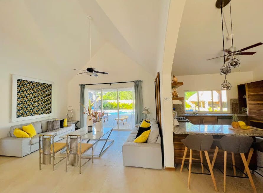 buyDRproperty Open-concept living area in a beautiful 9-bedroom villa with kitchen, sofas, and patio doors. Sosua Real Estate