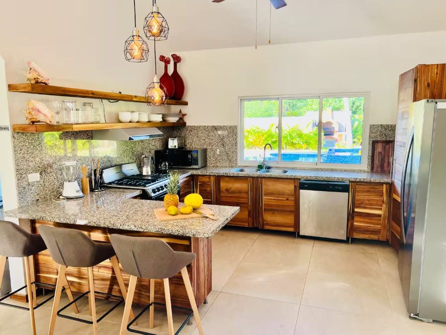 buyDRproperty Beautiful villa kitchen with granite countertops, wood cabinets, and fruit on the island. Sosua Real Estate