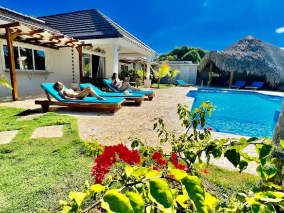 buyDRproperty Two women relaxing on sun loungers at a beautiful 9-Bedroom Villa with a pool. Sosua Real Estate