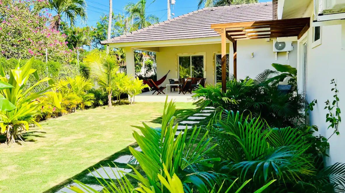 buyDRproperty Beautiful villa with a lush green lawn, tropical plants, and covered patio with outdoor seating. Sosua Real Estate