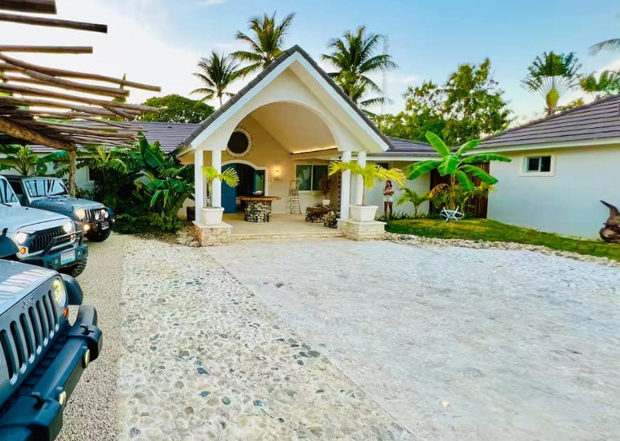 buyDRproperty Beautiful 9-Bedroom Villa exterior with Jeeps parked in the driveway, showcasing tropical landscaping and architecture. Sosua Real Estate