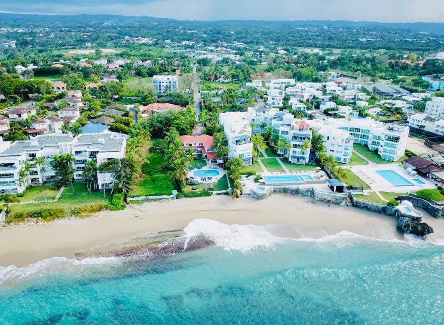 buyDRproperty Aerial view of a beautiful 9-bedroom villa near the beach with turquoise water and white condos. Sosua Real Estate