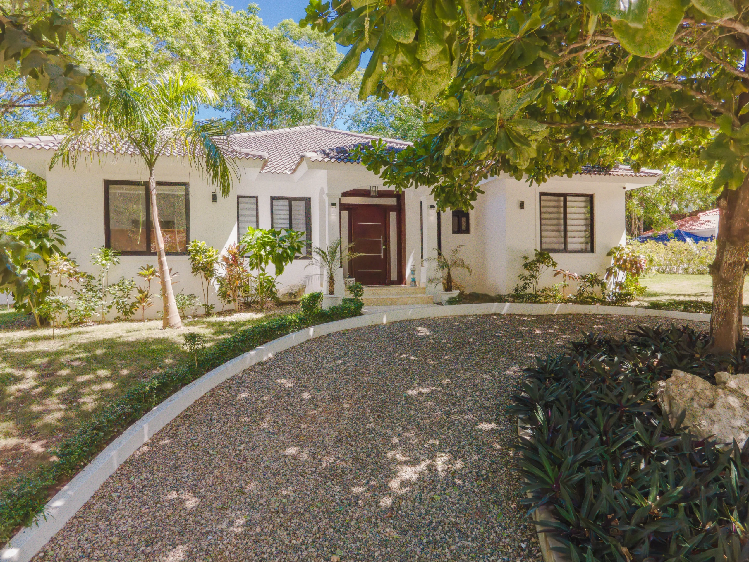 buyDRproperty Stunning white villa with gravel driveway and lush landscaping Sosua Real Estate