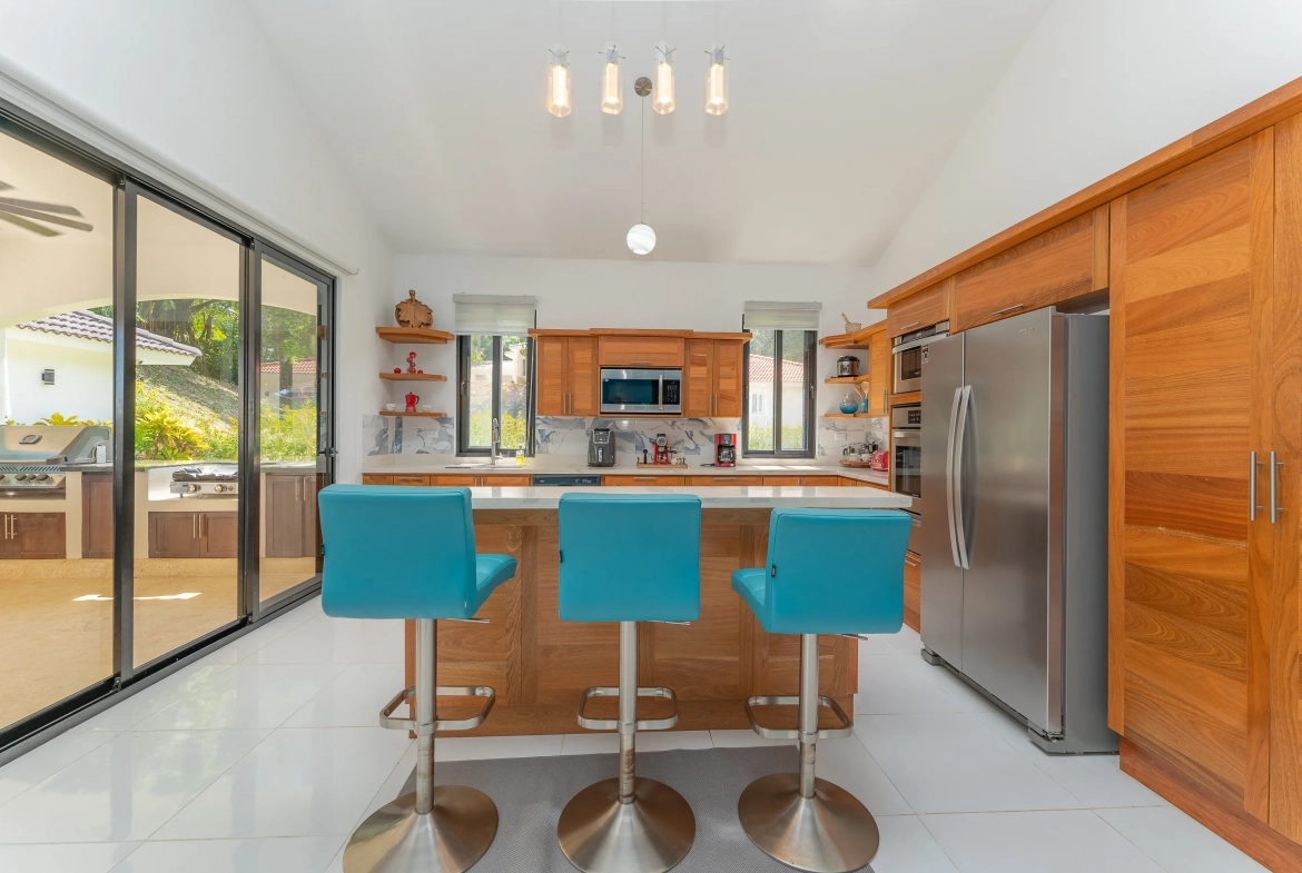 buyDRproperty Modern kitchen with blue bar stools, stainless steel appliances, and wooden cabinetry. Sosua Real Estate