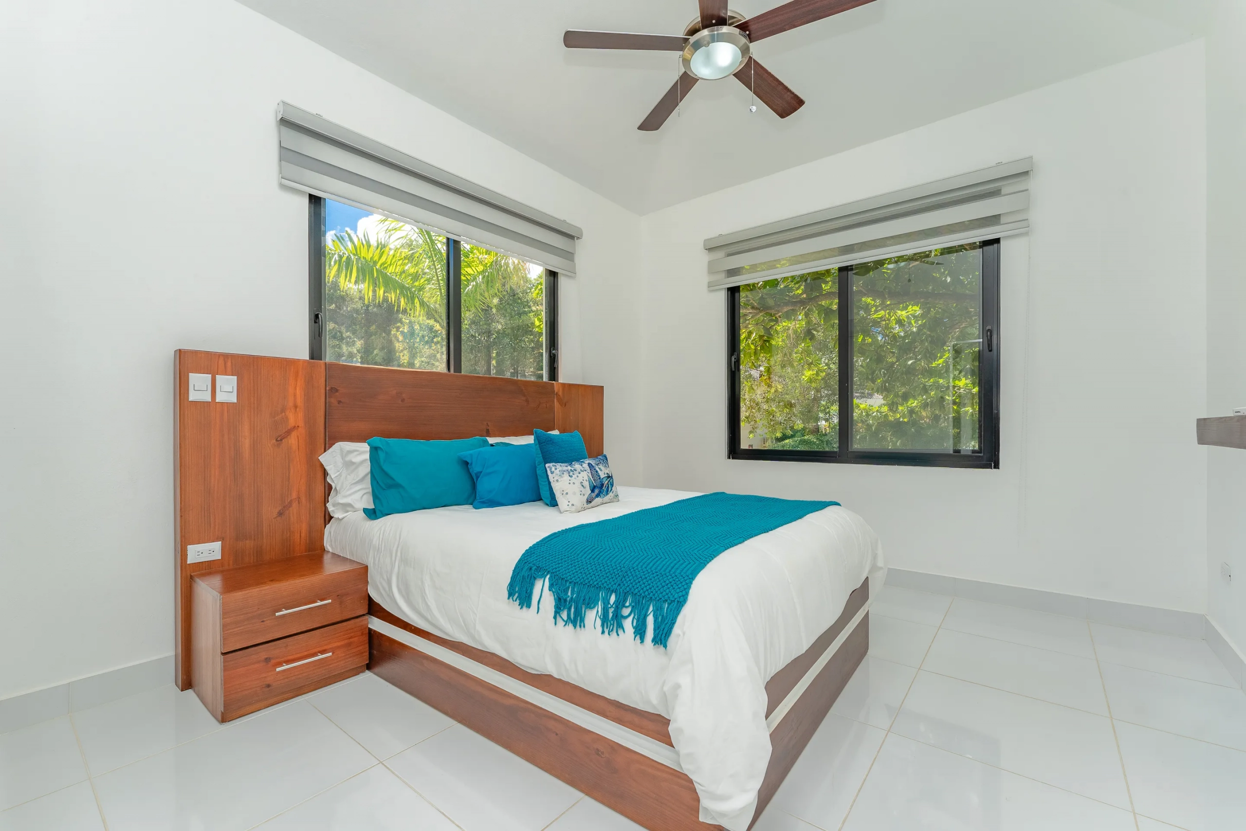 buyDRproperty Bedroom in a stunning villa with wooden bedframe, teal accents, and large windows. Sosua Real Estate