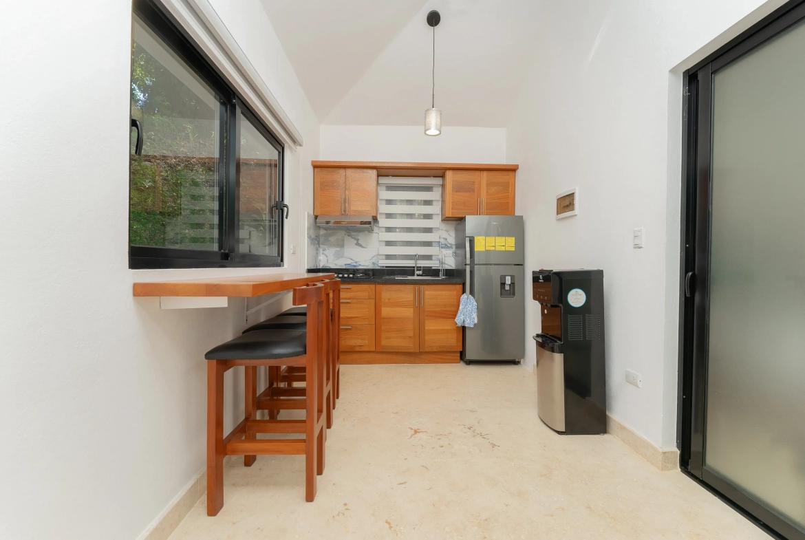 buyDRproperty Modern kitchen with wooden cabinets, countertop with stools, and stainless steel refrigerator. Sosua Real Estate