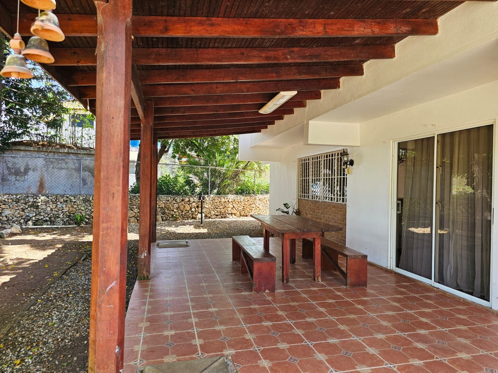 buyDRproperty Covered patio with wooden table and benches at this unique Sosua villa, tiled floor, and garden views. Sosua Real Estate