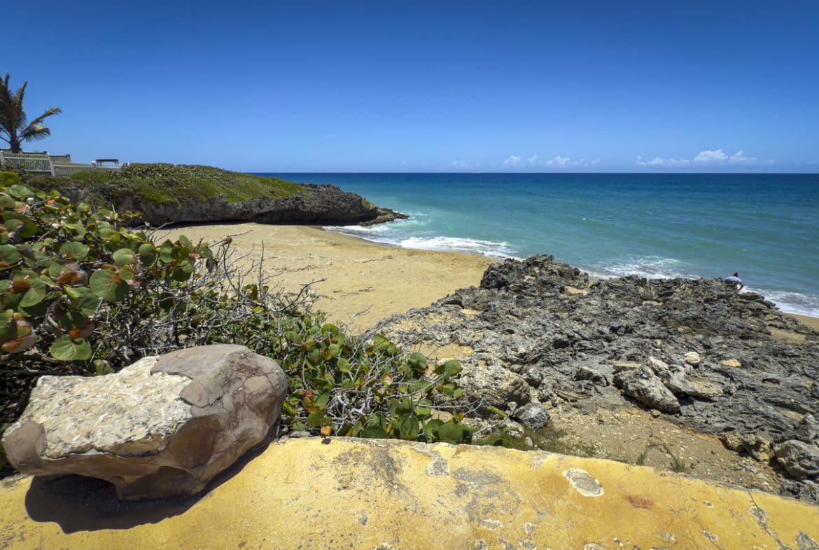 buyDRproperty Scenic coastal view with beach, rocks, and turquoise ocean under a clear blue sky. Sosua Real Estate