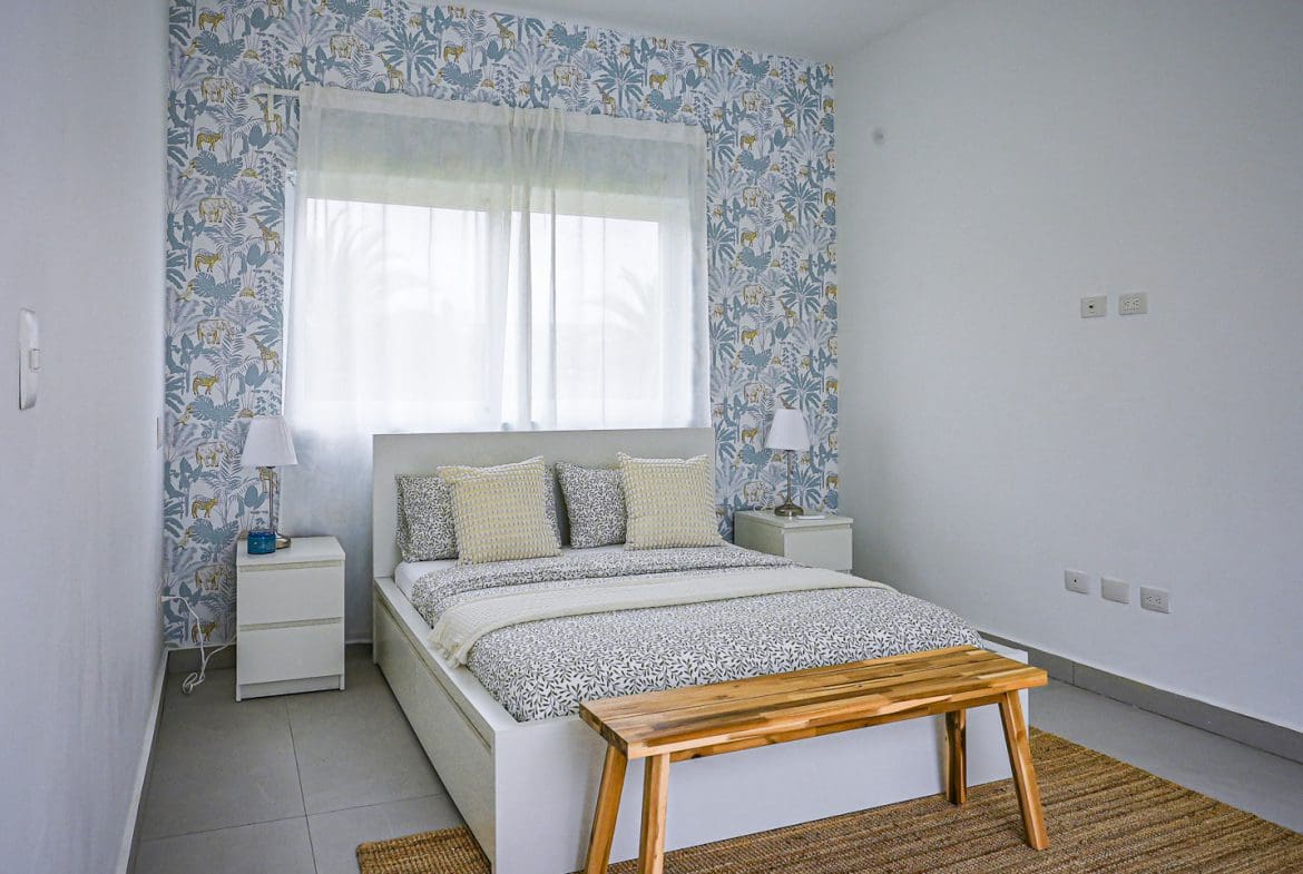 buyDRproperty Modern bedroom with patterned wallpaper, bed, and wooden bench. Sosua Real Estate
