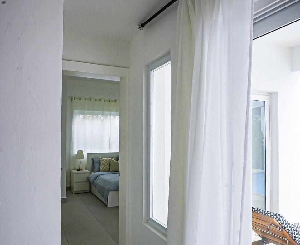 buyDRproperty Modern bedroom interior with sheer white curtains and a view of a lounge chair Sosua Real Estate