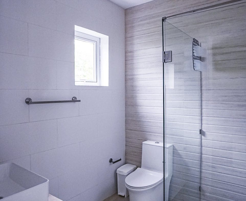 buyDRproperty Modern bathroom with white tile, glass shower, and toilet. Sosua Real Estate
