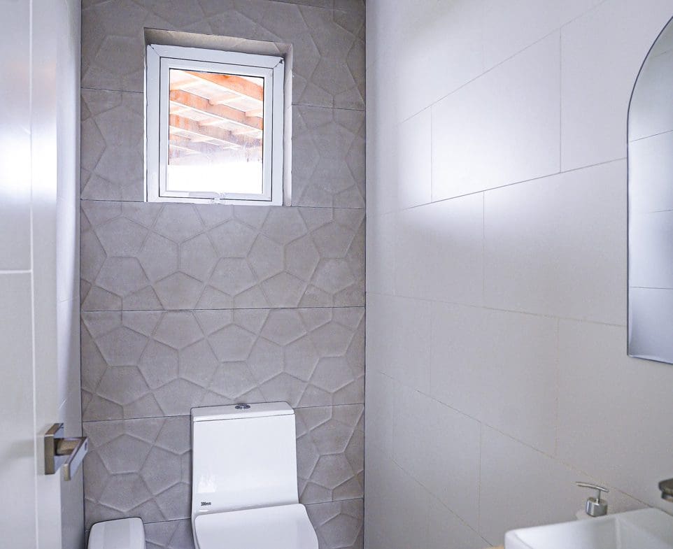 buyDRproperty Modern powder room with geometric tile accent wall, toilet, and small window. Sosua Real Estate