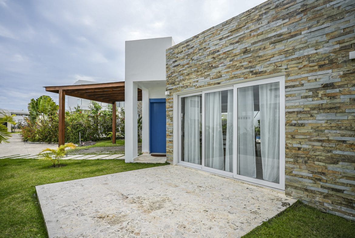 buyDRproperty Modern villa exterior with stone facade, sliding glass doors and blue door. Sosua Real Estate