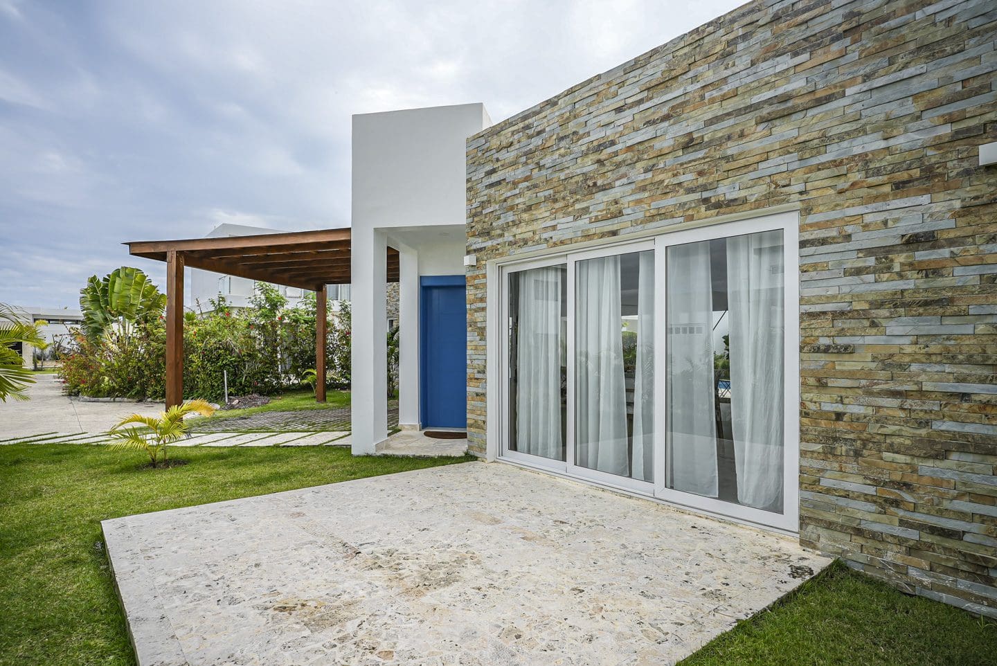 buyDRproperty Modern villa exterior with stone facade, sliding glass doors and blue door. Sosua Real Estate