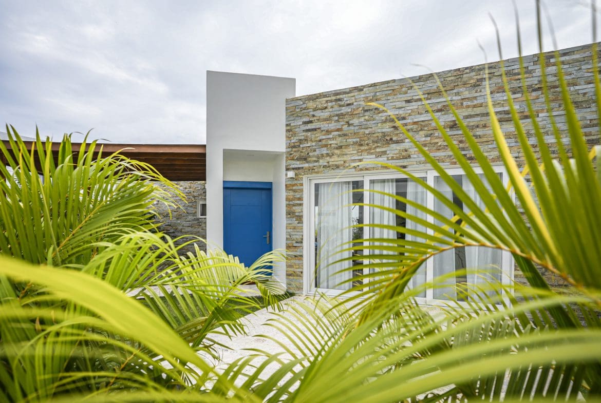 buyDRproperty Modern villa exterior with blue door and stone facade, surrounded by palm trees Sosua Real Estate