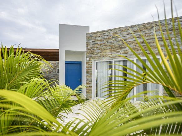 buyDRproperty Modern villa exterior with blue door and stone facade, surrounded by palm trees Sosua Real Estate