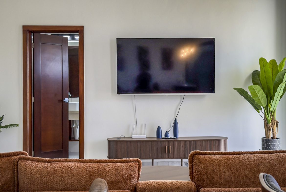 buyDRproperty Modern living room with TV, plants, and a glimpse of the bathroom in a Sosua Ocean Village villa. Sosua Real Estate