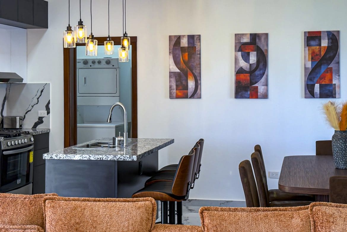 buyDRproperty Modern kitchen and dining area in a Sosua Ocean Village villa with island, artwork, and hanging lights. Sosua Real Estate