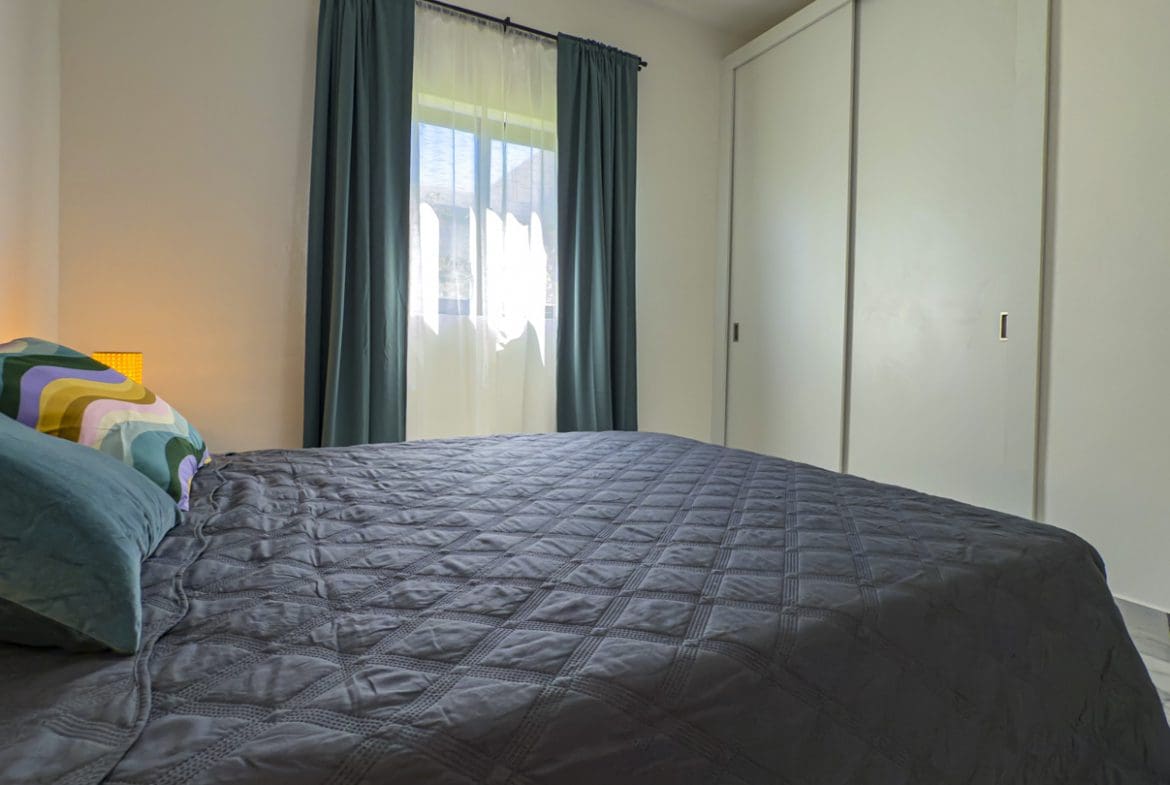 buyDRproperty Modern bedroom in a 3BR Villa Sosua Ocean Village with gray quilt and curtains. Sosua Real Estate