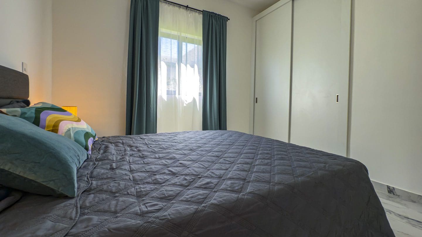 buyDRproperty Modern bedroom in a 3BR Villa Sosua Ocean Village with gray quilt and curtains. Sosua Real Estate