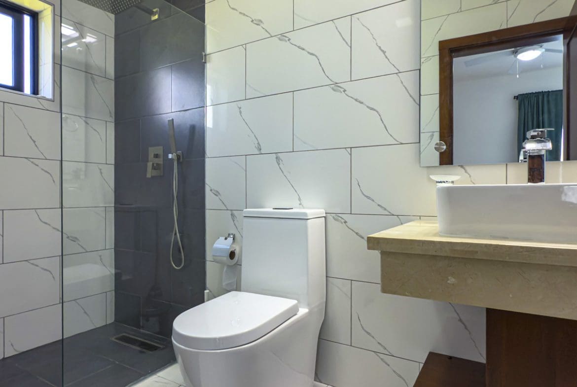 buyDRproperty Modern bathroom design in a Sosua ocean village villa featuring a sleek shower, toilet, and sink. Sosua Real Estate
