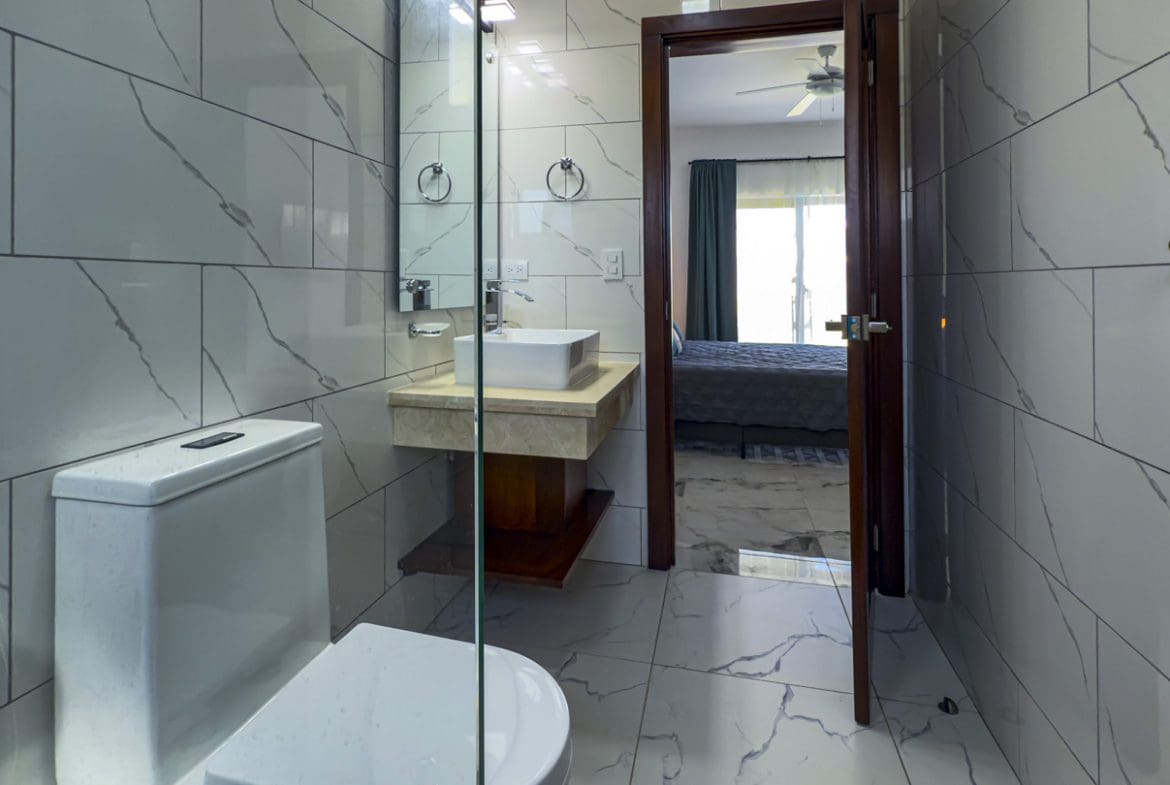 buyDRproperty Modern bathroom with marble tile, sink, and doorway to bedroom in a Sosua Ocean Village villa. Sosua Real Estate
