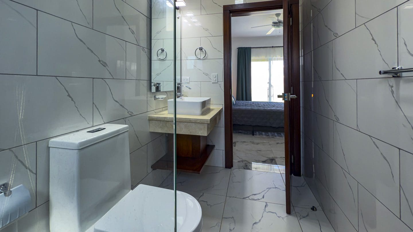 buyDRproperty Modern bathroom with marble tile, sink, and doorway to bedroom in a Sosua Ocean Village villa. Sosua Real Estate