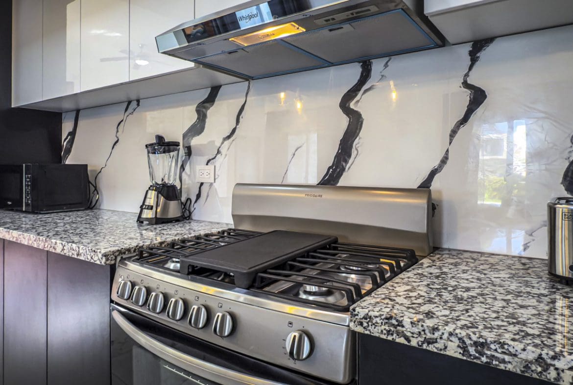 buyDRproperty Modern kitchen with stainless steel appliances, granite countertops, and marble-look backsplash. Sosua Real Estate